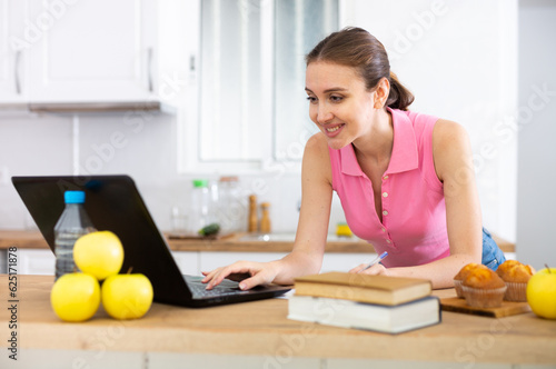 Woman cook reads the recipe in laptop and cooks salad in kitchen