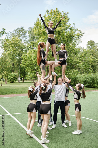 Vertical image of team of cheerleading training together with coach outdoors photo