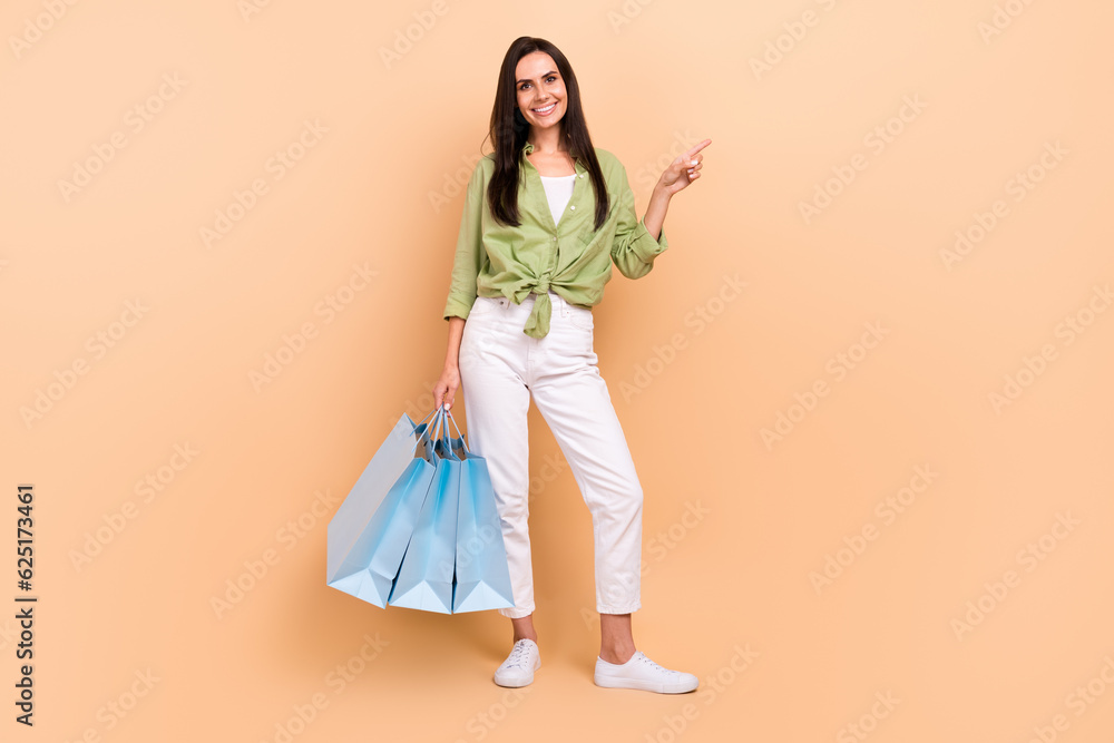 Full size photo of cheerful girl dressed green blouse trousers hold new outfit directing empty space isolated on beige color background Full size photo of cheerful girl dressed green blouse trousers hold new outfit directing empty space isolated on beige color background