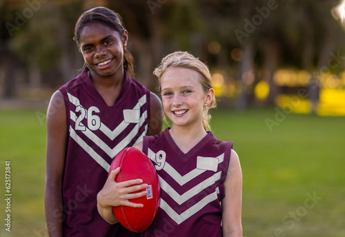 two school-aged girls in football jerseys holding aussie rules football photo