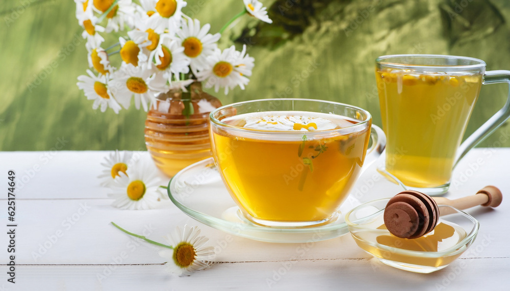 Chamomile herbal tea with flower buds, honey and lemon on a white wooden table and a bouquet of chamomile. Useful herbal, soothing drinks and natural healer concept. Immunity tea.Close up. Copy space. Chamomile herbal tea with flower buds, honey and lemon on a white wooden table and a bouquet of chamomile. Useful herbal, soothing drinks and natural healer concept. Immunity tea.Close up. Copy space.