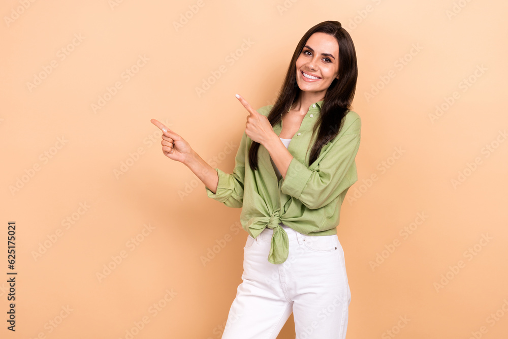 Photo of cheerful gorgeous girl toothy smile indicate fingers empty space information isolated on beige color background Photo of cheerful gorgeous girl toothy smile indicate fingers empty space information isolated on beige color background