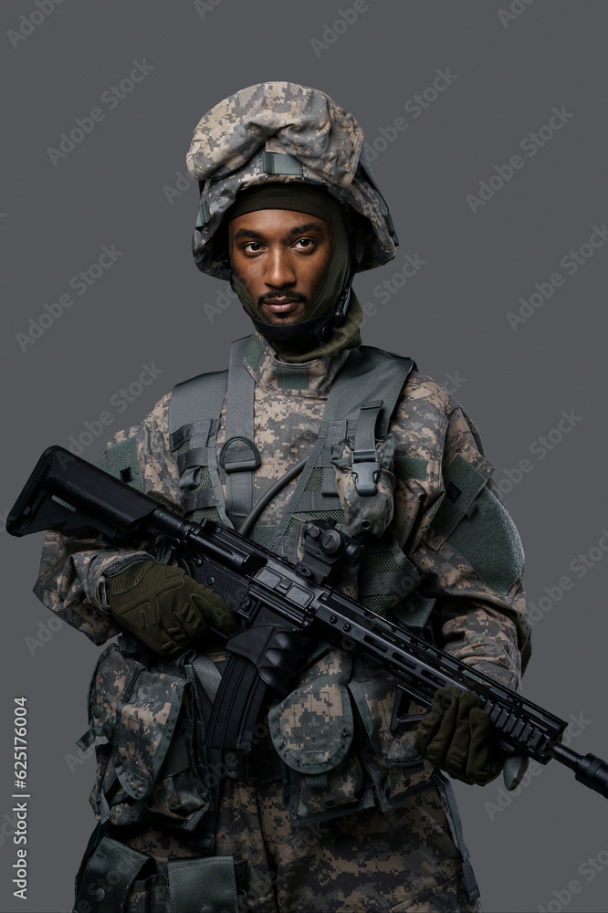 Confident soldier in NATO uniform and helmet poses with his rifle on a plain grey background, showcasing the courage and strength of military personnel