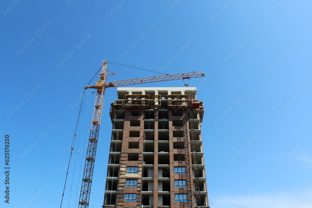 A high-rise building under construction stands against the blue sky with a crane.