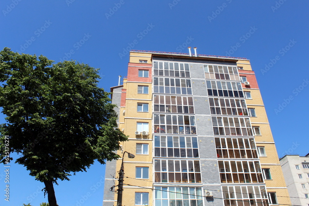 A high-rise multi-storey brick house stands against a blue sky, photo from bottom to top.	
