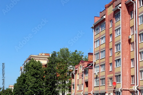 A high-rise multi-storey brick house stands against a blue sky  photo from bottom to top.