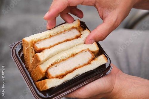 Unrecognizable person eating katsu sando, Japanese sandwich with pork cutlet, cabbage and tonkatsu sauce, at street. photo