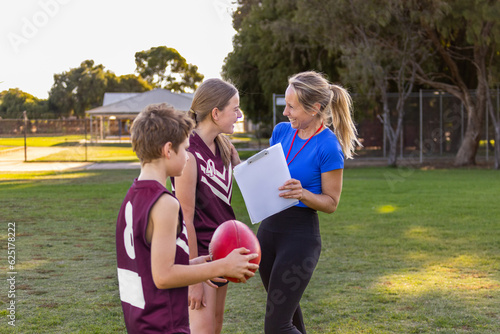 woman holding clipboard instructing children on football field