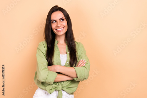 Photo of minded positive clever girl crossed arms toothy smile look empty space isolated on beige color background