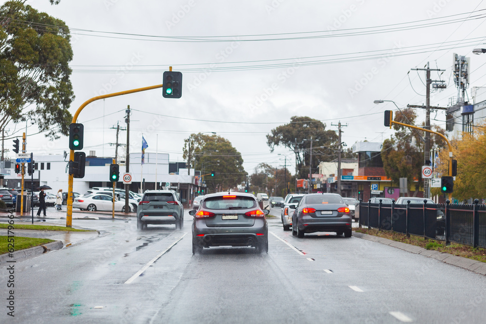 Traffic lights at intersection with cars on rainy wet day with slippery