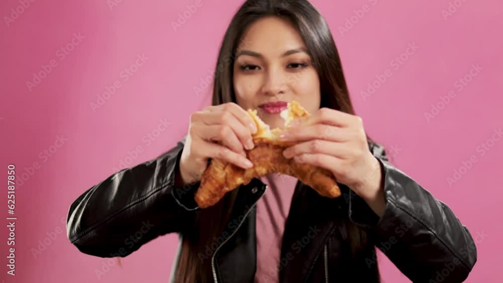 Asian Girl with a confident smile in a studio breaks a croissant for eating - extreme slow motion shot Asian Girl with a confident smile in a studio breaks a croissant for eating - extreme slow motion shot