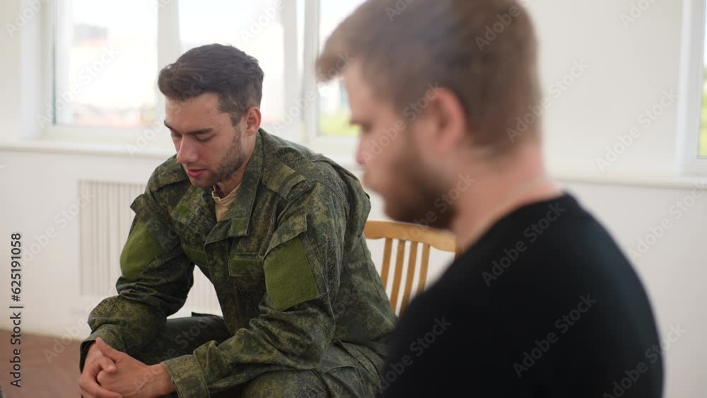 Dramatic view of young bearded veteran male in camouflage uniform with disability attending PTSD support group speaking about his experience. Concept of mental health, psychotherapy, social issues. Dramatic view of young bearded veteran male in camouflage uniform with disability attending PTSD support group speaking about his experience. Concept of mental health, psychotherapy, social issues.