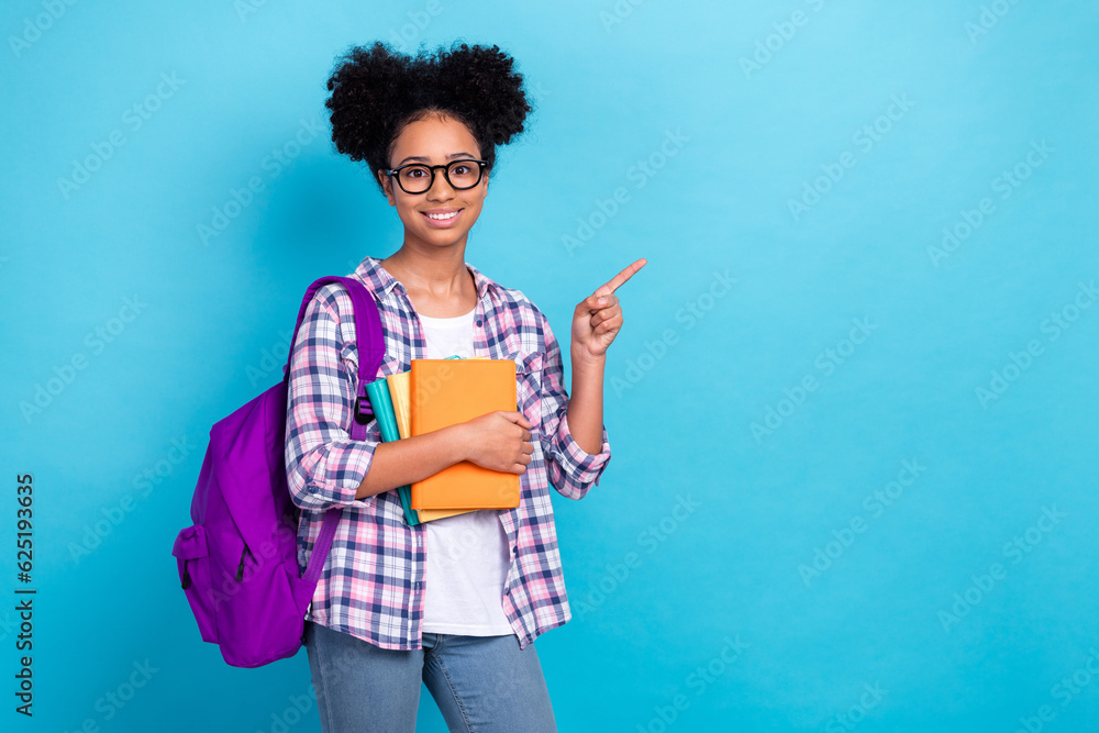 Portrait of diligent teenager with afro hairstyle wear plaid shirt hold book directing empty space isolated on blue color background Portrait of diligent teenager with afro hairstyle wear plaid shirt hold book directing empty space isolated on blue color background