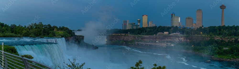 Large panoramic of Niagara Falls, NY and Ontario, Canada, water falls and viewing areas with buildings and cityscape seen in Canada across niagara river in the early morning light