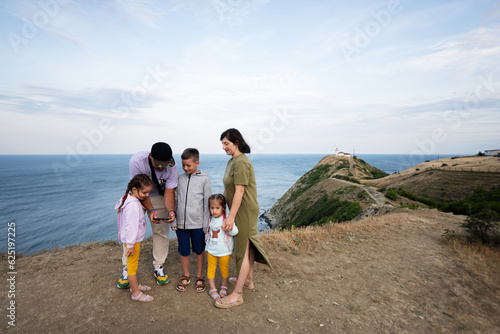 Family of five standing on top of the mountain and looking on phone screen against sea. Cape Emine, Black sea coast, Bulgaria.