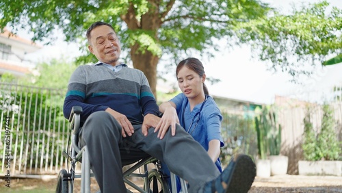 Young asian woman physical therapists helping elderly male patient in wheelchair making leg and knee physiotherapy. Symptom knee pain of elderly 