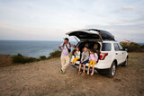 Family sitting on the back of a suv car at the beach against lighthouse. Cape Emine, Black sea coast, Bulgaria.