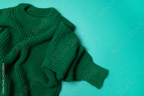 Green knitted sweater on paper green background top view copy space. Texture of woolen cotton winter autumn cozy sweater, clothes. Knitted jumper, pullover, fashion. Sweater close-up