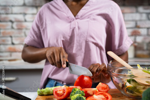 Young African woman in kitchen. Close up of woman making salad.