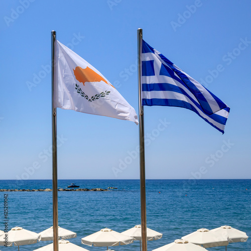National flags of Cyprus and Greece fluttering in front of blue sea, sky and beach umbrellas