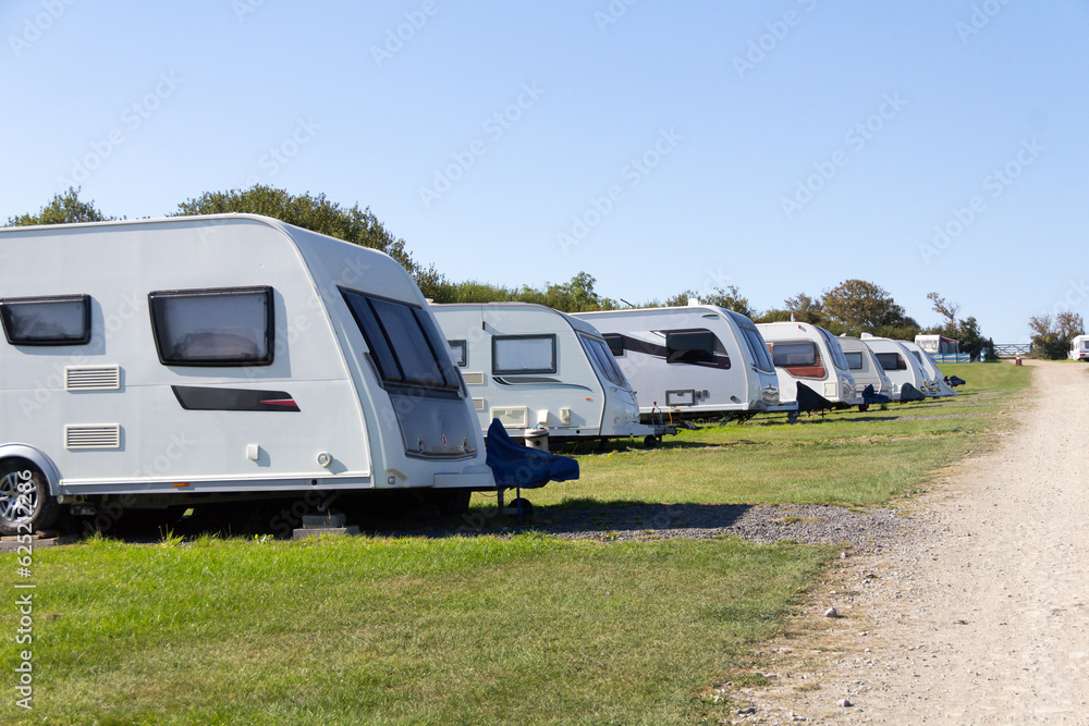 Row of caravans parked up on grass in Caravan Park as holiday makers enjoy their vacations on a summers day .