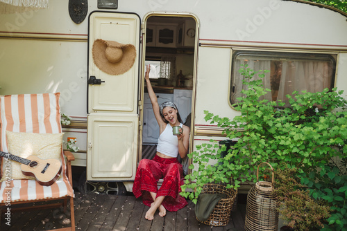 Happy hippie girl are having a good time with cup of tea in camper trailer. Holiday, vacation, trip concept.