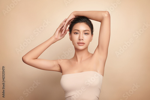 Beautiful Young Asian woman lifting hands up to show off clean and hygienic armpits or underarms on beige background, Smooth armpit cleanliness and protection concept photo