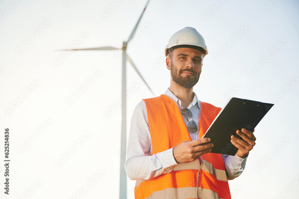 Black notepad in hands. Service engineer is on the field with windmills Black notepad in hands. Service engineer is on the field with windmills