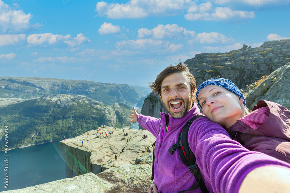 Couple taking a selfie on a rock and admiring a view on Preikestolen. Aerial shot, upper perspective on the couple. Endless view of the fjord.