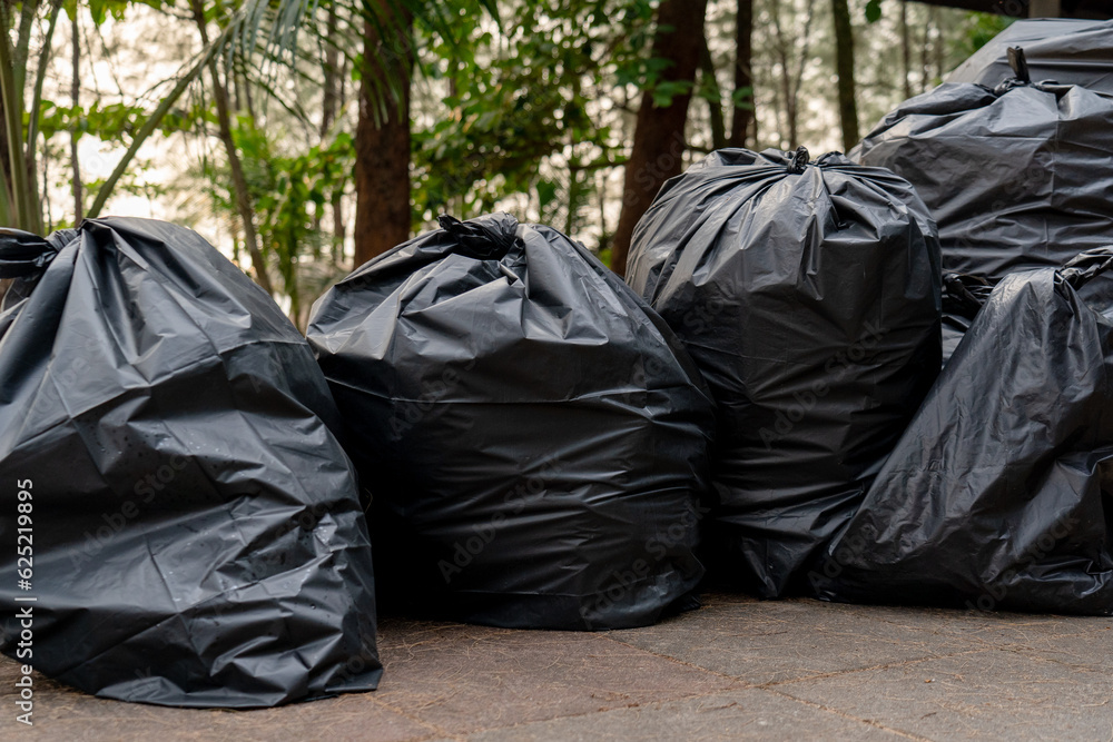 pile of disposable black garbage bags placed on ground around camping area full of trash separated wet waste and plastic for recycling, volunteer cleaning beach for protecting the environment