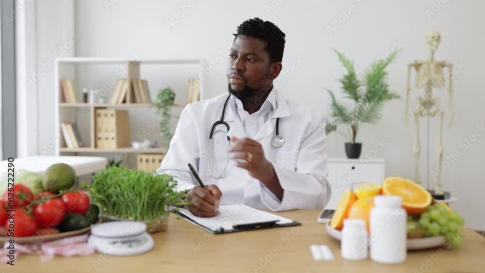 Doctor gastroenterologist filling patient's case history and prescribing recipe wile sitting at work desk full of fruits and vegetables. Male professional writing vegetable diet plan in clinics.