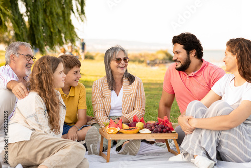 Glad caucasian multi-generation people relax outdoor, enjoy picnic, food and weekend in park