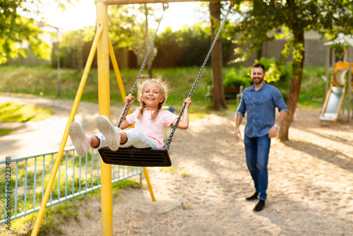 Happy european family of father and daughter spending time at playground, playing and dad pushing child on the swing #625223418