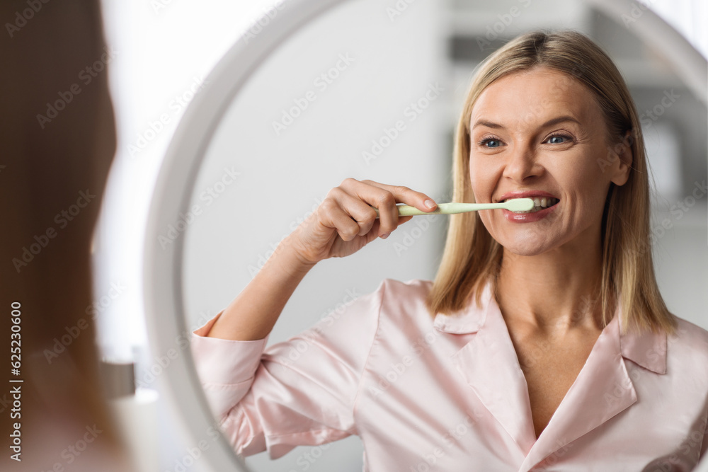 Beautiful Mature Female Brushing Her Teeth With Toothbrush Near Mirror At Home Beautiful Mature Female Brushing Her Teeth With Toothbrush Near Mirror At Home