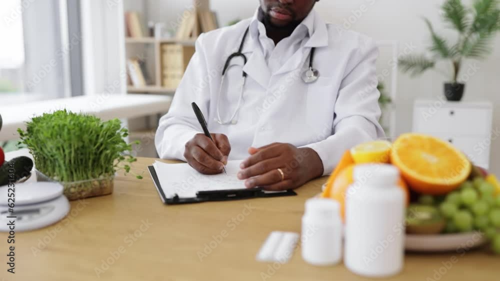Expert in nutrition making special menu for patient and writing list of allowed products on clipboard paper during work time in hospital. African american man touching chin with hand and thinking. Expert in nutrition making special menu for patient and writing list of allowed products on clipboard paper during work time in hospital. African american man touching chin with hand and thinking.