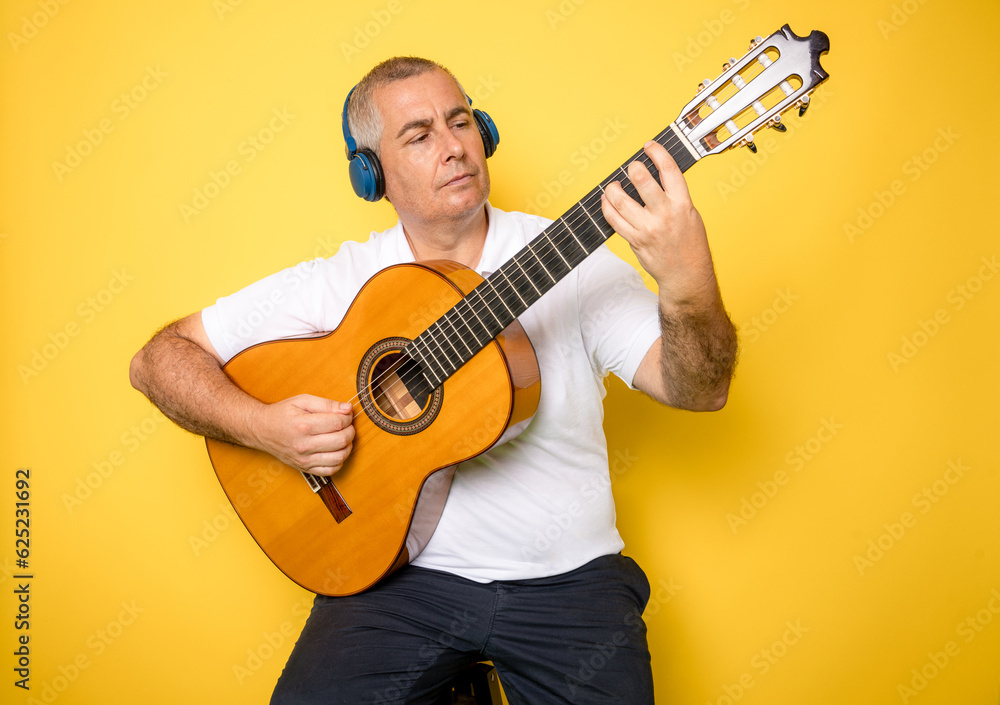 Obraz premium Man wearing headphones playing guitar isolated over yellow background