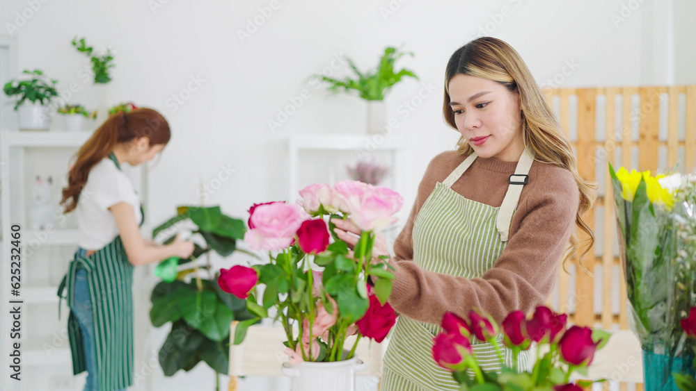 Young asian woman florist in apron working in flower shop. Concentrated young female florist arranging flowers in shop. Small business concept