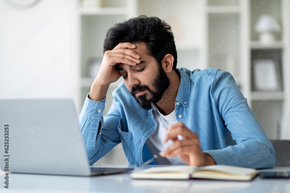 Overworking. Tired Indian Man Sitting At Desk With Laptop And Touching Head Overworking. Tired Indian Man Sitting At Desk With Laptop And Touching Head