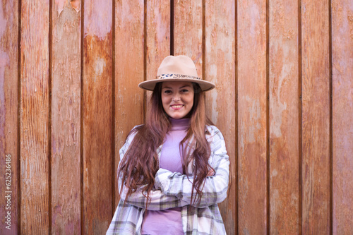 Young and beautiful Spanish woman from Seville with brown hair, hat and checkered shirt standing on a wooden door in different poses and expressions.