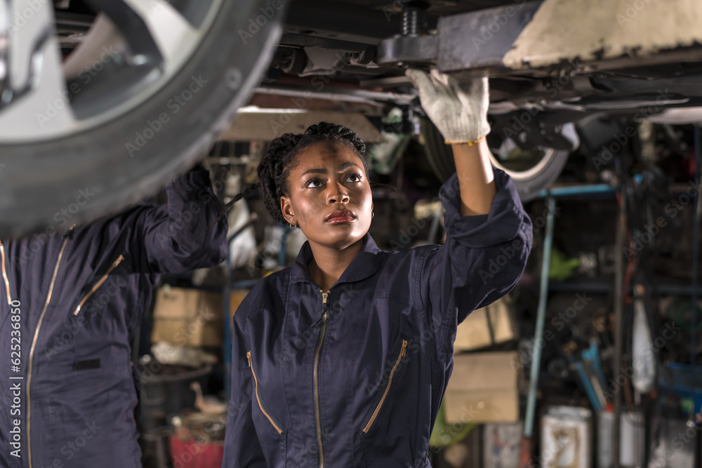 Black Car Mechanic woman doing car maintenance underneath vehicle in auto repair shop