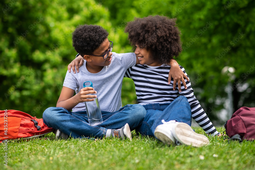 Two african american kids sitting on the grass in the park