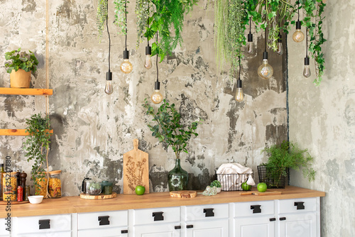 Interior scandi open cuisine. Wooden shelves with various cookware, plants in pots and decoration in the kitchen. Loft pendant Edison light bulbs lamps on background of rough cement plaster on wall.  photo