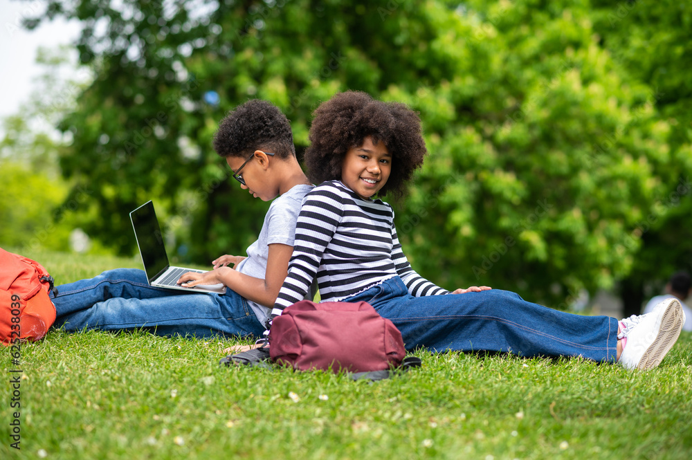 Two curly-haired teens sitting on the grass in the park and feeling good Two curly-haired teens sitting on the grass in the park and feeling good