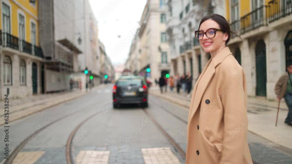 Attractive young woman in beige coat crossing street, holding her smartphone, looking sideways and smiling. Young lady wearing horn-rimmed glasses enjoying autumn day in European city. Follow shoot Attractive young woman in beige coat crossing street, holding her smartphone, looking sideways and smiling. Young lady wearing horn-rimmed glasses enjoying autumn day in European city. Follow shoot