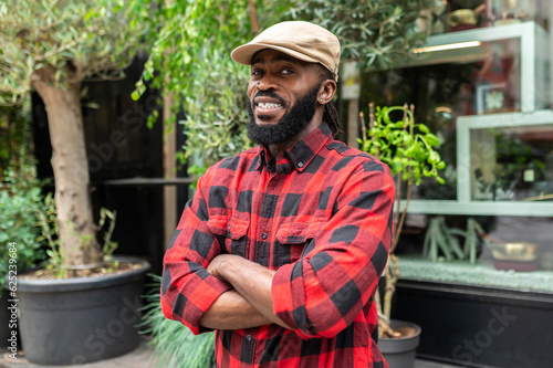Young man in cap and in plaid red shirt standing on a greenery background