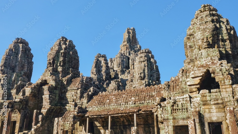 General view of the Bayon Temple in Cambodia on a sunny day, stone towers with human faces.