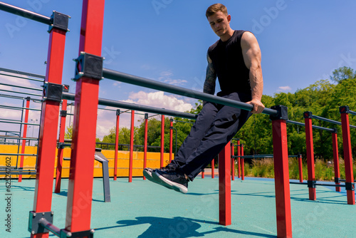 portrait of a young sportsman working out on parallel bars swinging his arms and shoulders doing push-ups on sports ground during street training