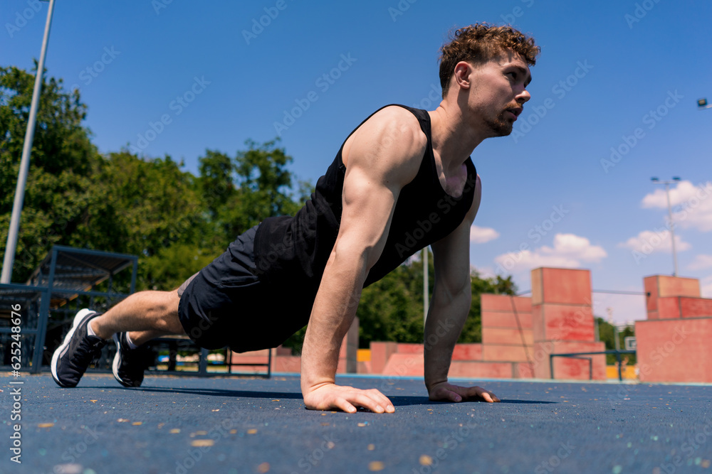 Fototapeta premium young pumped-up athlete doing push-ups from the ground during street training endurance exercise swings arms and shoulders