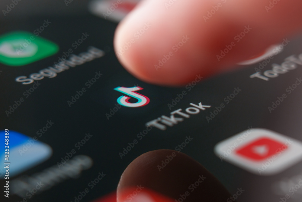 Tik tok app logo on smartphone screen with pressing finger Stock Photo