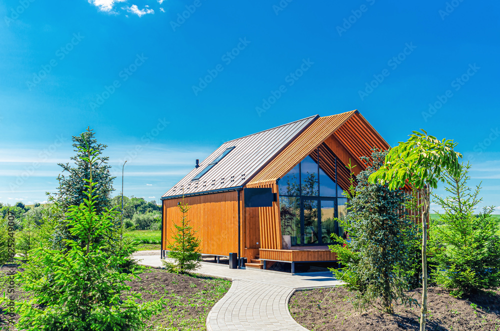 Small barnhouse house on a plot with a path, trees and bushes under a blue sky Small barnhouse house on a plot with a path, trees and bushes under a blue sky